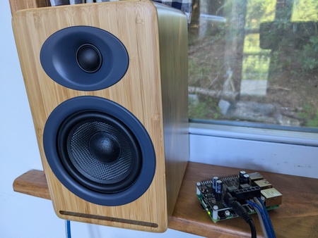 Picture of a Bookshelf speaker with a bamboo case and 2 black speakers mounted in it. On the side is a Raspberry Pi with a audio amplifier mounted on top 